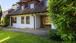 Ein zweistöckiges Haus mit geneigtem Dach, einer Veranda und einem gepflegten Garten.