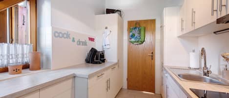 A modern kitchen with white cabinets, a wooden door, and a countertop with a coffee maker.