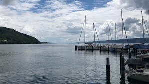 A calm lake with sailboats docked at a pier, surrounded by hills.
