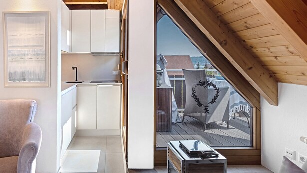 A modern kitchen with white cabinets, a wooden ceiling, and a view of a balcony with outdoor furniture.