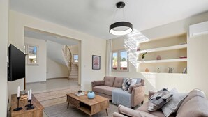 Una sala de estar moderna con un sofá, una mesa de centro y un televisor. Se ve una escalera que sube a otro nivel.