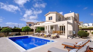 Una villa moderna con piscina, tumbonas y una zona de estar cubierta al aire libre.