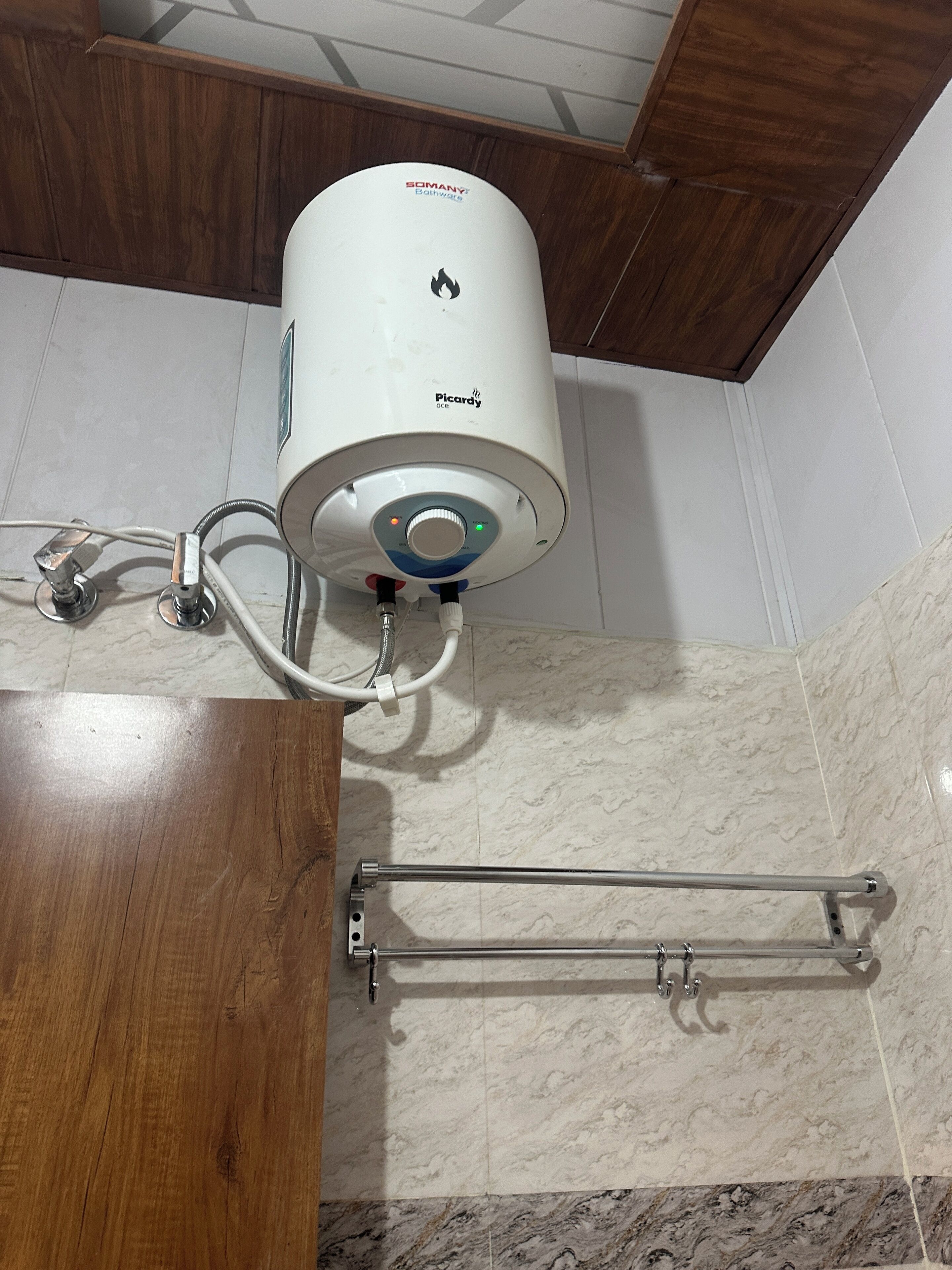 A bathroom with a water heater mounted on the wall, a towel rack, and a wooden vanity.