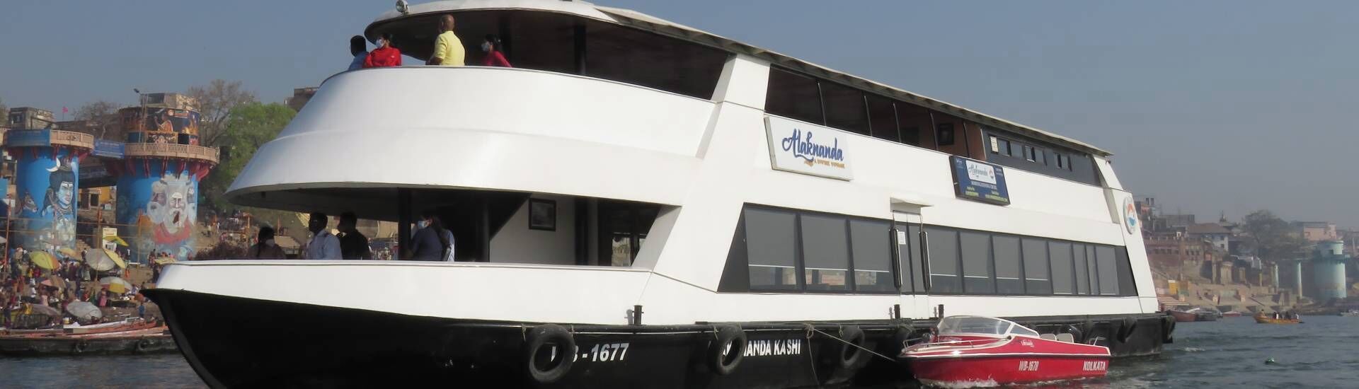 A white river cruise boat with a deck area and a smaller red boat docked alongside.