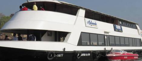 A white river cruise boat with a deck area and a smaller red boat docked alongside.