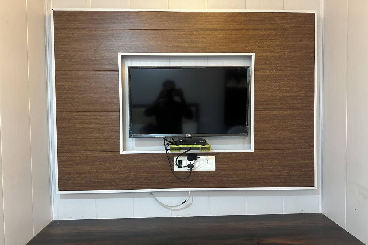 A television mounted on a wooden panel wall with a white frame, connected to a power outlet below.