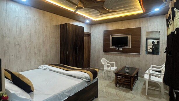 A modern hotel room with a wooden ceiling, a bed with white linens, a small table with a glass, and a TV mounted on the wall. - Ganga Godawari Guest House (Varanasi)