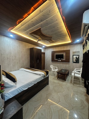 Una habitación de hotel moderna con techo de madera, una cama con ropa blanca, una mesita con un vaso y un televisor montado en la pared.