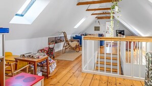 Ein geräumiges Dachzimmer mit hohen Decken, Holzbalken, einer Treppe und einem Oberlicht.