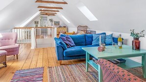 Ein Loft-Zimmer mit blauem Sofa, Holzbalken, einem Holztisch und einem farbenfrohen Teppich.