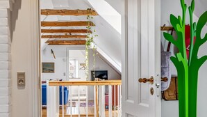 Ein Flur mit Holzboden, einer weißen Tür mit einer Zimmerpflanze und Blick in einen Raum mit Bett und Fernseher.