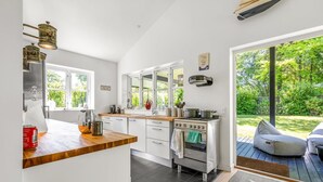 Una cocina moderna con armarios blancos, encimera de madera y estufa integrada. Amplias ventanas ofrecen luz natural y vistas al jardín.