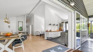 Amplia sala de estar con mesa de comedor, sofá y zona de cocina con refrigerador y lavaplatos.