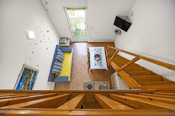 A room with a wooden staircase, a sofa, a table, and a TV on the wall.