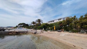 A coastal area with a clear water body, a sandy beach, and a building with a balcony overlooking the water. - Serene Studio by the Sea (Banjol)