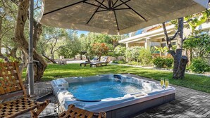 A hot tub with two glasses of champagne, surrounded by wooden chairs and an umbrella, set on a wooden deck with a grassy lawn and trees in the background. - Serene Studio by the Sea (Banjol)