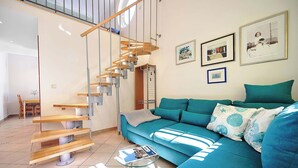 A modern living room with a wooden staircase, a teal sofa, and a glass coffee table.