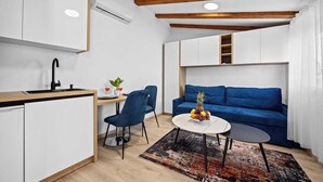 Un espacio habitable pequeño con kitchenette, un sofá azul, una zona de comedor con mesa y sillas, y una alfombra pequeña.