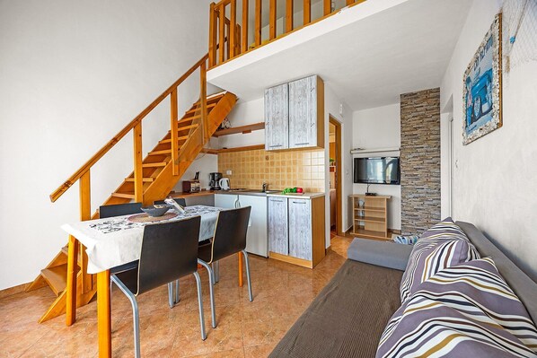 Une cuisine compacte avec un coin repas, un escalier et un salon doté d’un canapé.