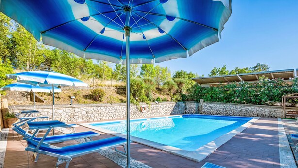 A pool area with multiple lounge chairs and umbrellas, surrounded by stone walls and greenery. - La Rocca by Interhome (Magione)
