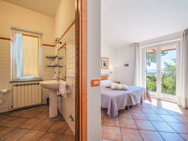 A bathroom with a sink, mirror, and window, and a bedroom with a bed, window, and balcony.
