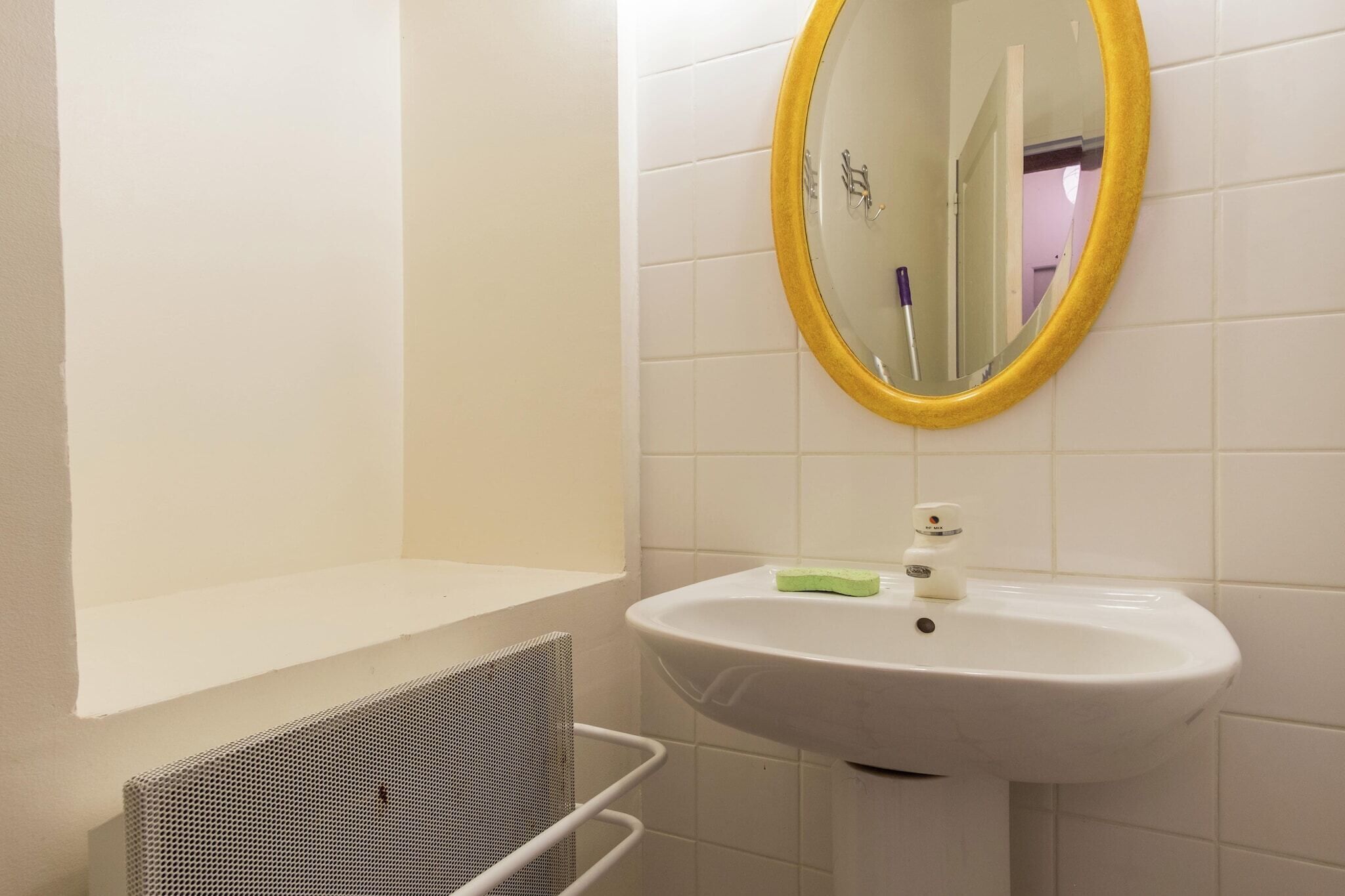 A bathroom with a white sink, a yellow-framed mirror, and a white towel rack.