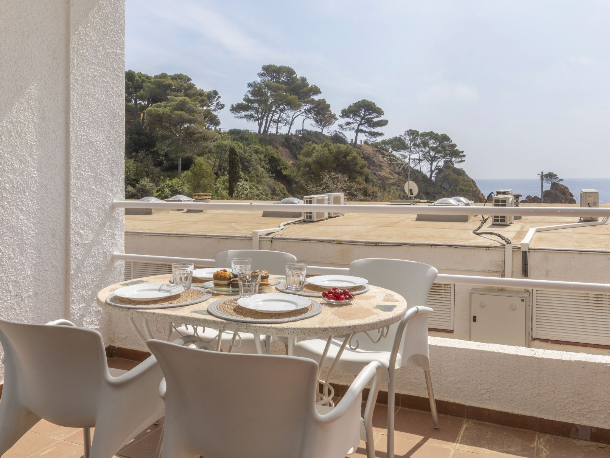 Eine Terrasse mit Esstisch, mit Blick auf eine malerische Landschaft mit Bäumen und Meerblick.