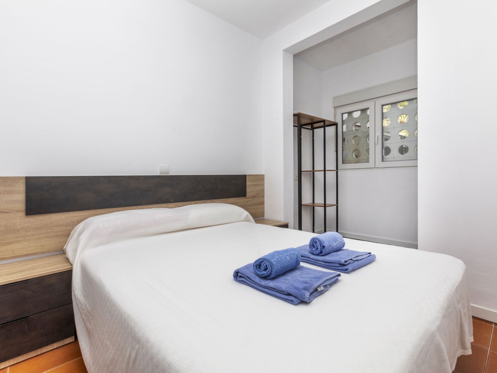 Ein Hotelzimmer mit Bett, Holz-Kopfteil, Fenster mit dekorativem Metallrahmen und integriertem Regal.