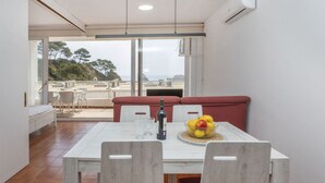 A modern dining area with a white table, red cushioned bench, and a bowl of fruit. - AirMenuda by Interhome (Tossa de Mar)