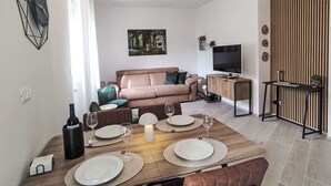 Ein modernes Wohnzimmer mit einer Couch, einem Esstisch für vier Personen, einem Fernseher und einer Wandpaneinung aus Holz.