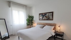 Ein modernes Schlafzimmer mit einem großen Bett, einem Nachttisch mit Lampe, einem Spiegel und einem Bild an der Wand.