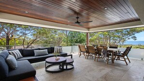 A covered outdoor seating area with a sofa, round table, and chairs, overlooking a scenic view. - Beautiful ocean views, beaches and bushwalks (MACMASTERS BEACH)