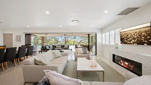 A modern living room with a fireplace, a dining area, and a view of the outdoors. - Beautiful ocean views, beaches and bushwalks (MACMASTERS BEACH)