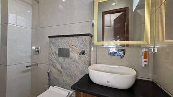 A modern bathroom with a marble wall, a large mirror, a white sink, and a toilet.