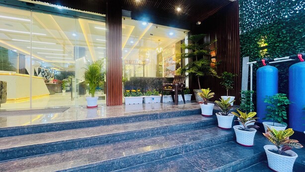 A hotel entrance with steps leading to a reception area, potted plants, and a glass facade with interior lighting. - The Castle View (Haridwar)