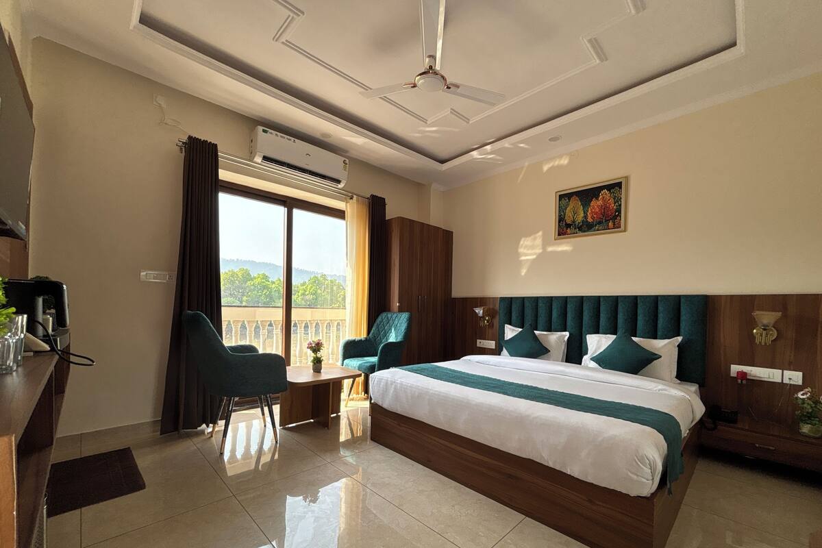 Une chambre d’hôtel avec un grand lit, un bureau, une chaise et un balcon offrant une vue sur les collines.