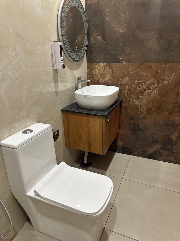 A bathroom with a white toilet, a sink with a marble countertop, and a mirror with a decorative frame. - The Castle View (Haridwar)