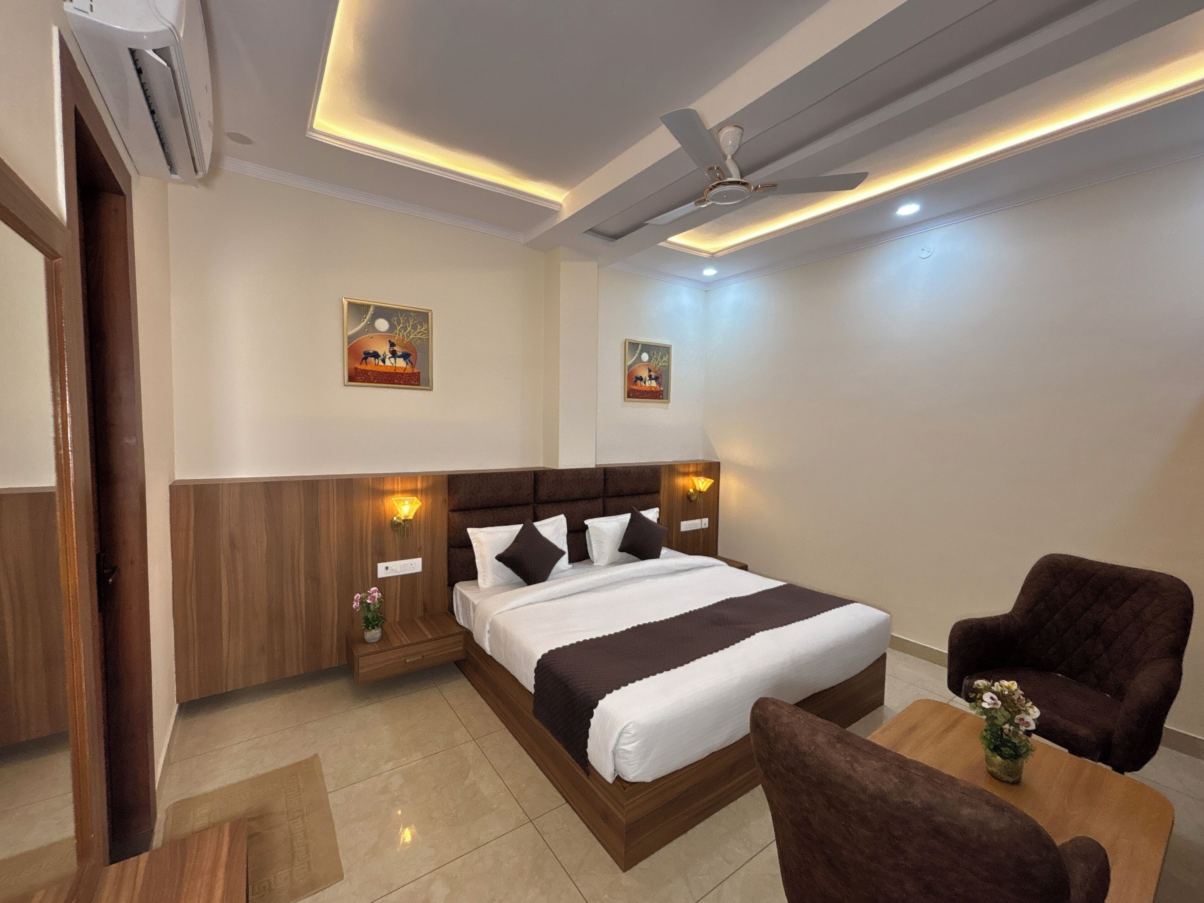 A hotel room with a bed, two wall-mounted lamps, a ceiling fan, and two framed pictures on the wall.