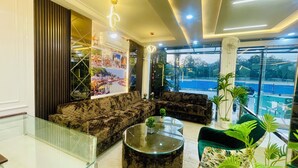 A modern hotel lobby with a sectional sofa, a glass coffee table, and a view of the street through large windows. - The Castle View (Haridwar)