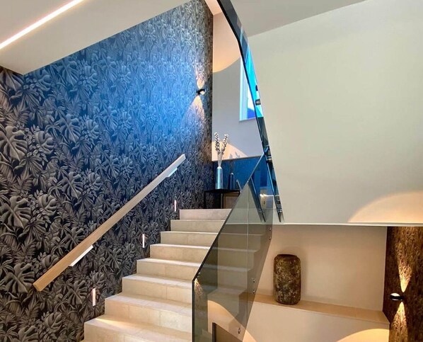 A modern staircase with a glass railing, a blue floral wall, and a wooden accent piece. - Villa Four Seasons Ljubac (Ražanac)
