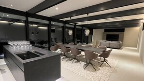 A modern kitchen with a central island, dining area with chairs, and a seating area with a sofa and TV. - KISIN (Yoichi)