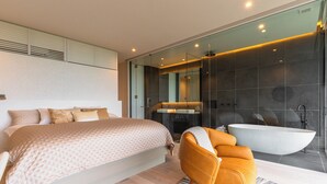 A modern bedroom with a large bed, a bathroom with a bathtub, and a seating area with a chair. - KISIN (Yoichi)