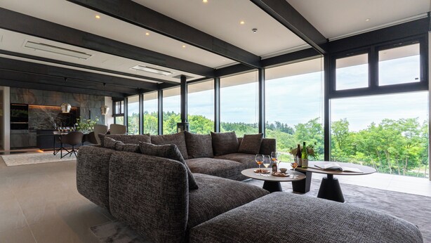 A modern living room with a sectional sofa, a round coffee table, and a view of the outdoors. - KISIN (Yoichi)
