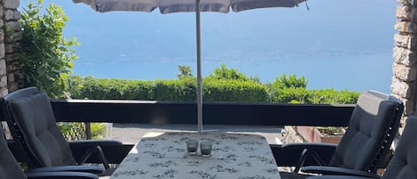 Eine Terrasse mit Tisch, Stühlen und Sonnenschirm, mit Blick auf das Meer.