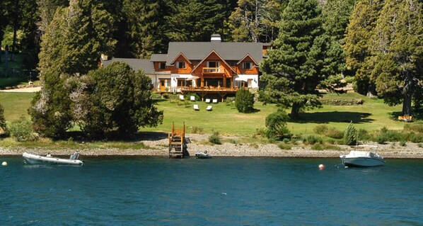 Una amplia casa de madera con terraza, rodeada de árboles y un lago.