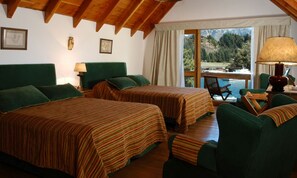 Habitación con dos camas, cabeceros tapizados en verde, techo de madera y vista a un lago, además de una mesa con lámpara.