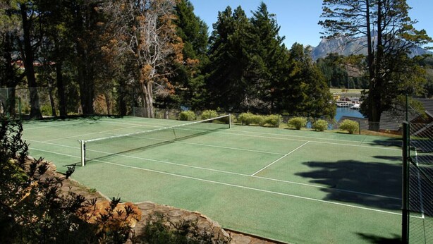 Een tennisbaan omgeven door bomen met een berg op de achtergrond.