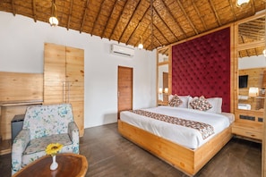 A room with a wooden bed, a floral armchair, a wooden nightstand, and a mirror. - The Corbett Selva Resort by DevStayZ (Ramnagar)
