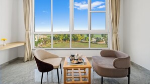 A room with a large window, two chairs, a small table with a tray of food, and a vase with flowers. - Corbett Selva Resort By DevStayz -Pet-Friendly Resort (Ramnagar)