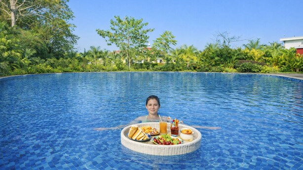 A person in a swimming pool with a floating tray containing food and drinks. - Corbett Selva Resort By DevStayz -Pet-Friendly Resort (Ramnagar)
